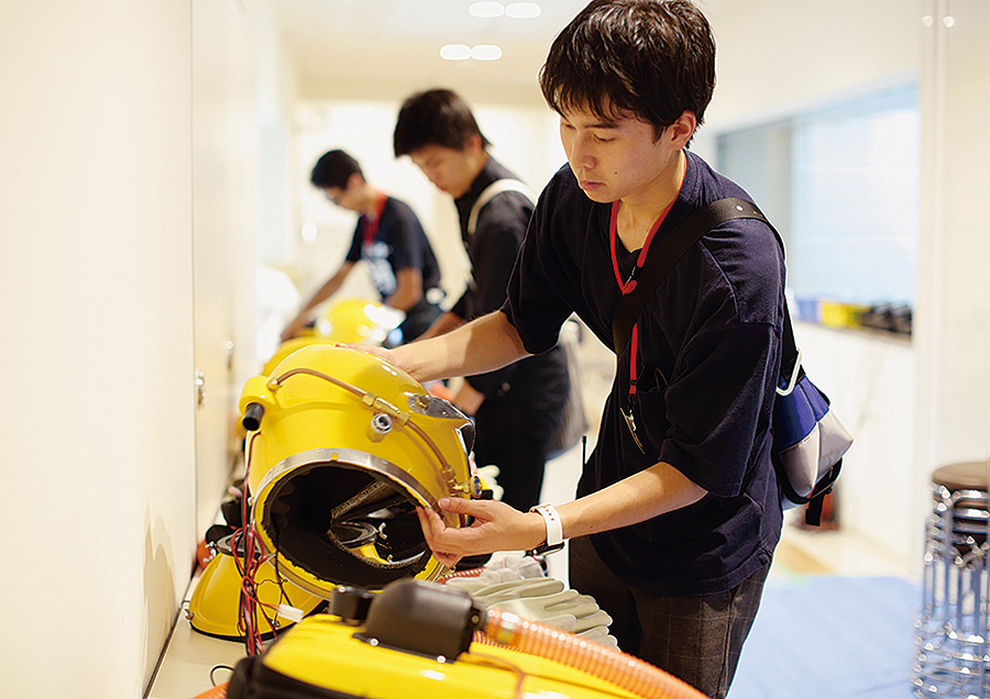 スタッフとして撮影に携わっている学生たちが、撮影現場をフォローしている様子。黄色の防護服は『BOLT』で使用されたヤノベケンジさんのアート作品の一部。