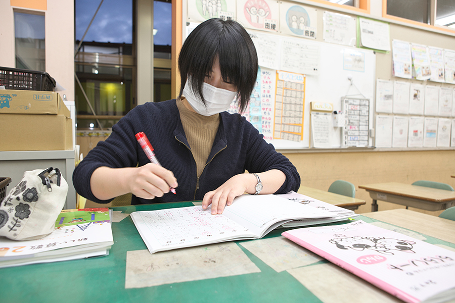 日本画コース卒業生で小学校教諭の小見七望さん 子どもたちの自習ノートに丸付けをする